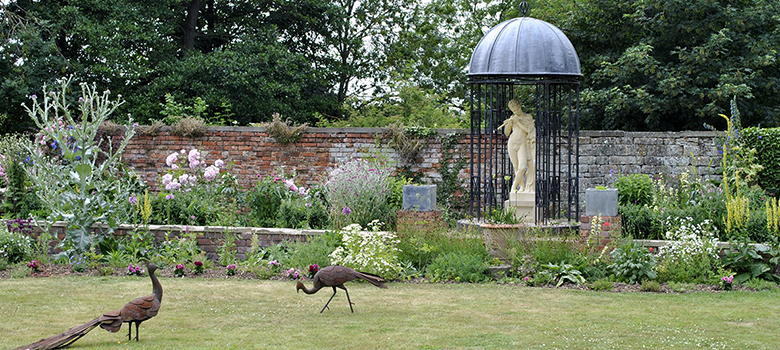 A view across the gardens including sculpture and a well-stocked walled garden bed.