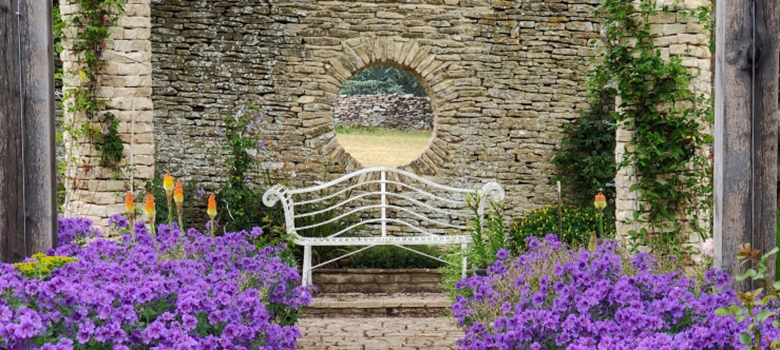 Well-stocked garden beds lead you to a seating place with a moon window to the lawn beyond.